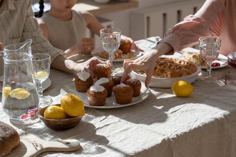 A family gathering around a sunny table with lemonade, cupcakes, and citrus fruits, creating a warm and inviting atmosphere.