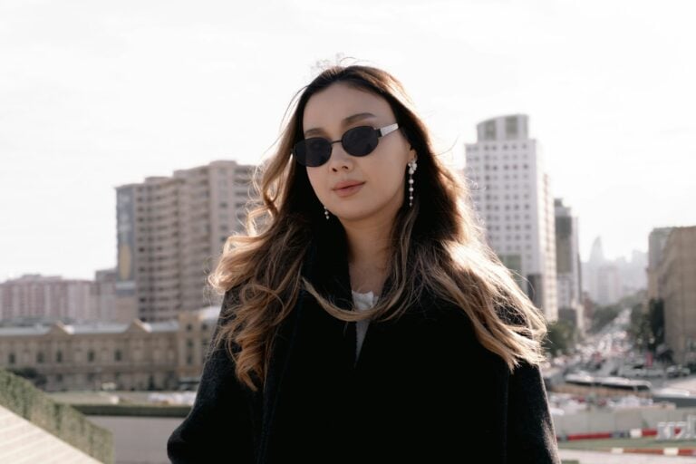 Stylish woman wearing sunglasses with city buildings behind.