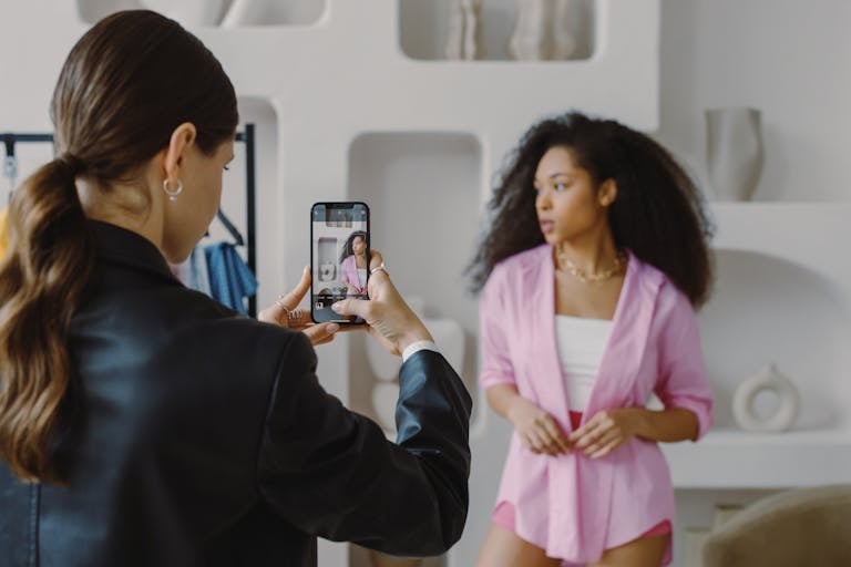 A woman uses a smartphone to photograph a model posing indoors. Modern and creative.
