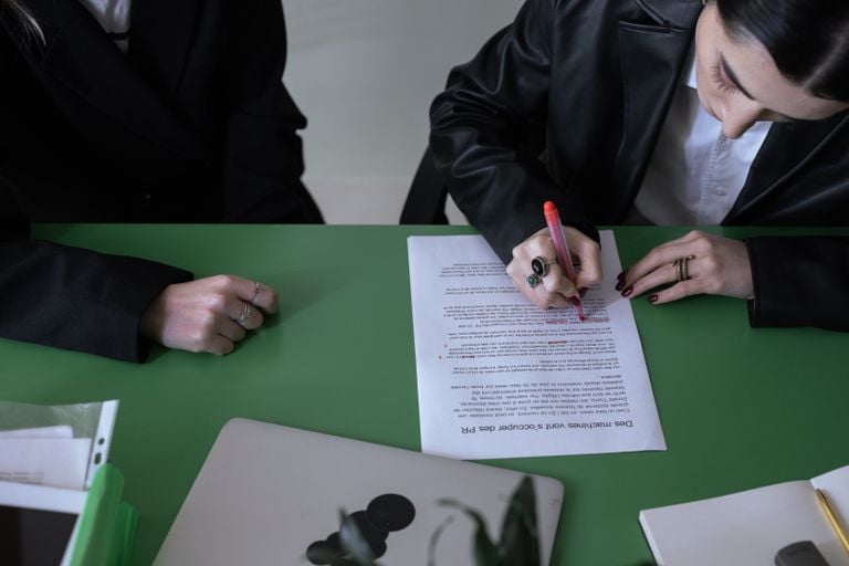 A woman marking a document with a red pen at a green desk.